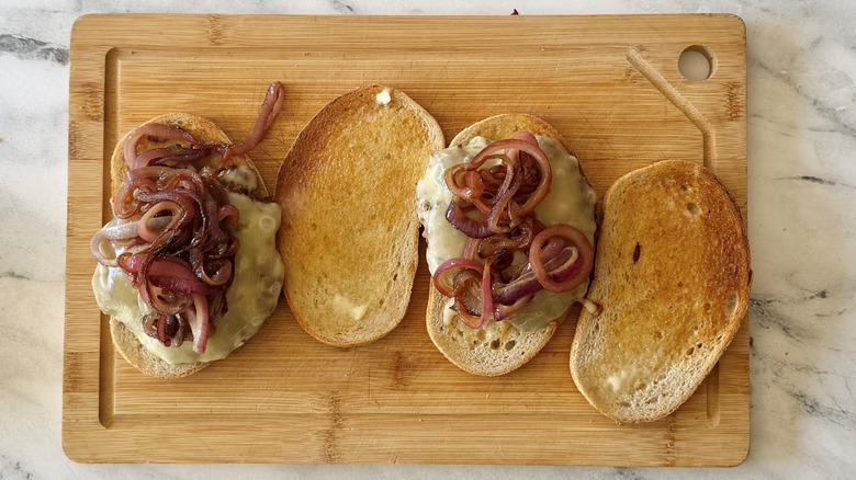 Open faced patty melts with grilled onions on wooden board