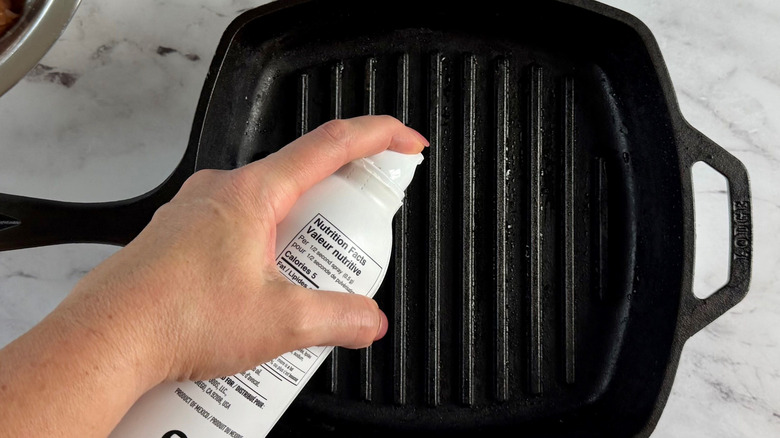 Hand spraying grill pan with cooking spray