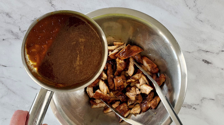 Sauce pouring into bowl of sliced chicken