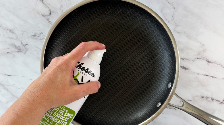 Hand holding cooking spray over pan