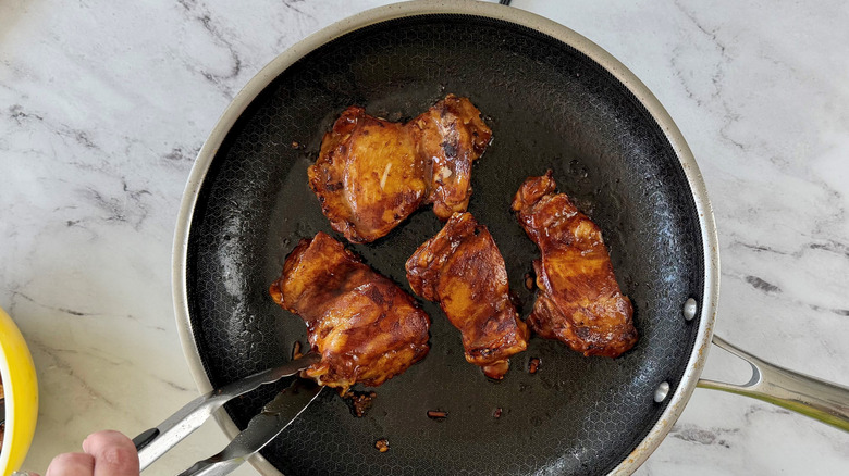 Tongs flipping chicken in pan
