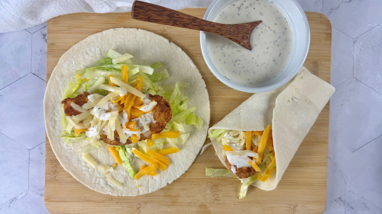 Unwrapped and wrapped chicken snack wraps and bowl of ranch on wooden board