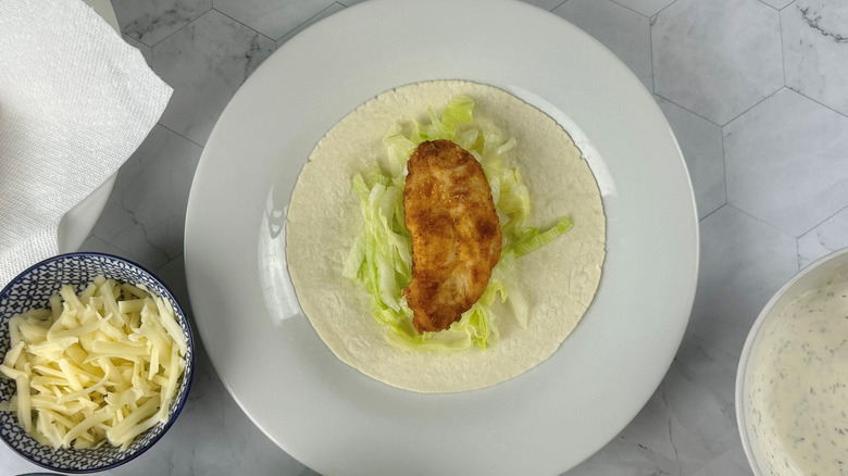 Chicken tender and lettuce on tortilla on plate