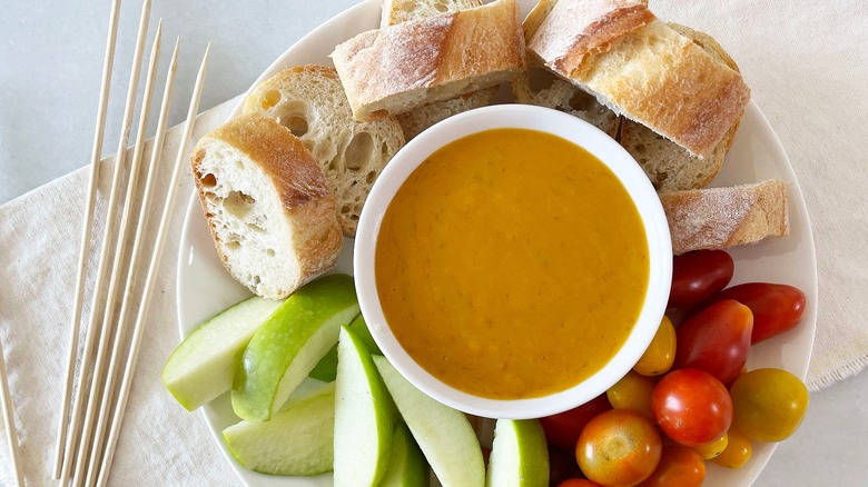 cheese fondue served with bread, apples, and tomatoes