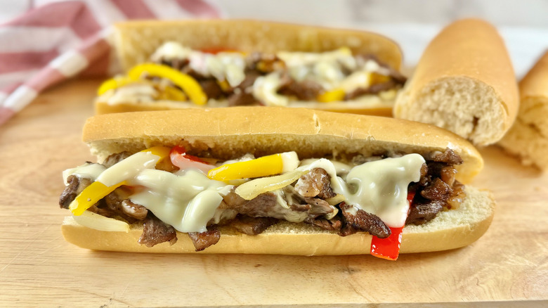 steak and cheese sandwich with bell peppers on a wooden board in front a striped napkin