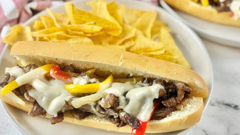 steak and cheese sandwich with bell peppers on a white plate with potato chips