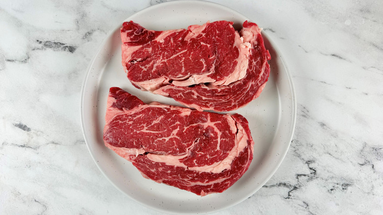 two raw steaks on a white plate