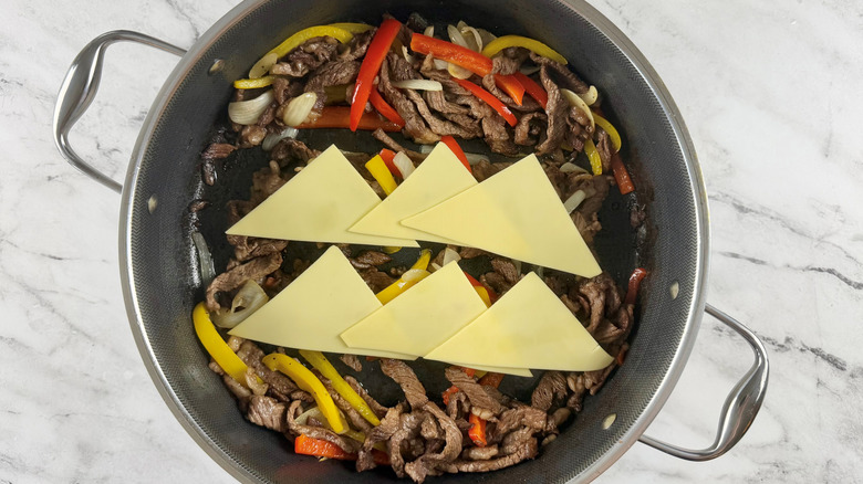 cooked meat, vegetables, and cheese in a black frying pan