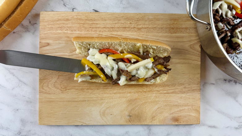 knife sticking out of a steak, cheese, and bell pepper sandwich