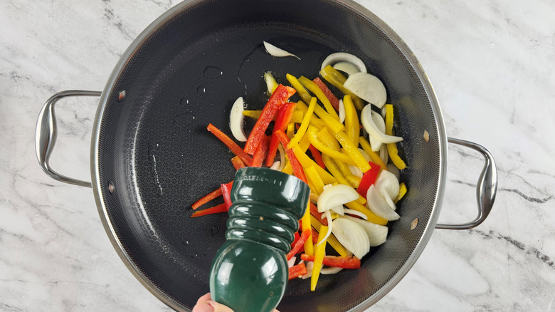 hand holding a large green salt or pepper grinder over a frying pan full of vegetables