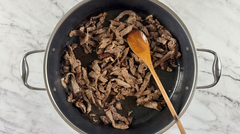 cooked meat in a black frying pan with a wooden spoon