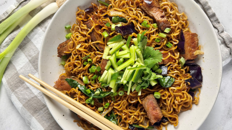 ramen noodles with steak strips and green onions in a white bowl