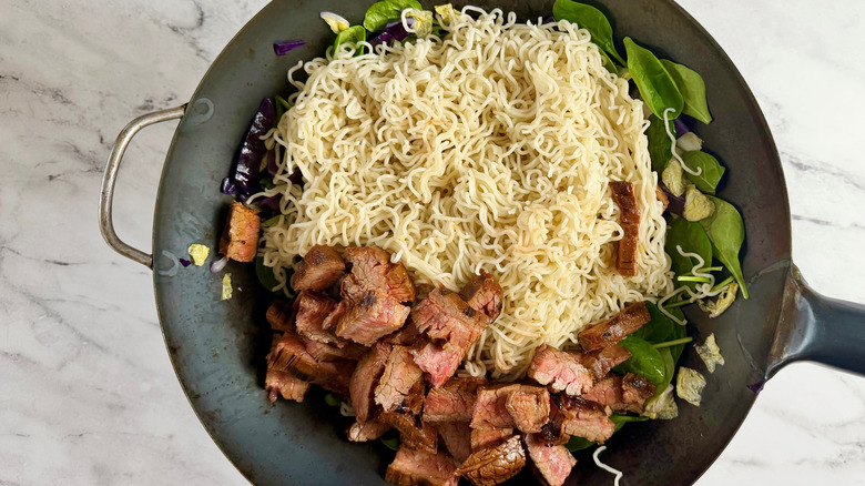 noodles, steak,  and vegetables in a round pan
