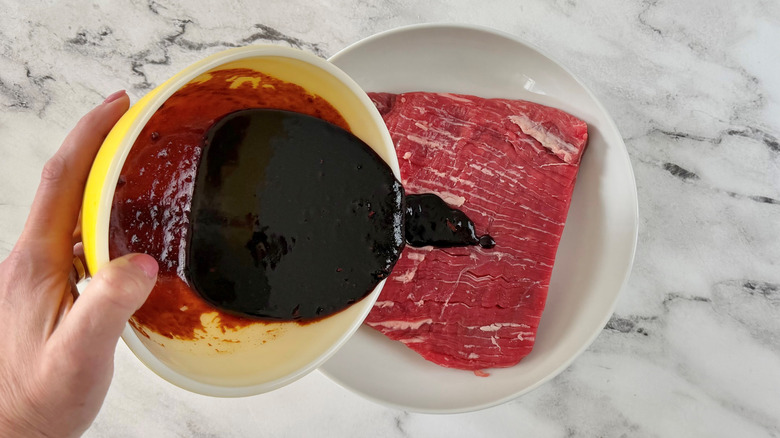 hand pouring brown liquid over raw steak
