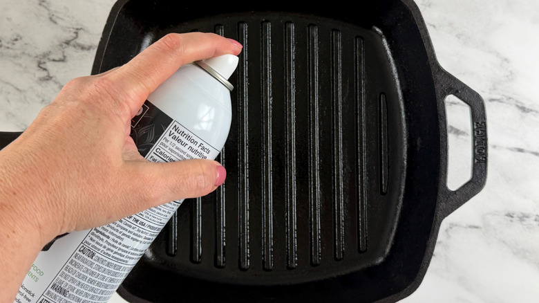 hand holding an aerosol can above a square black frying pan