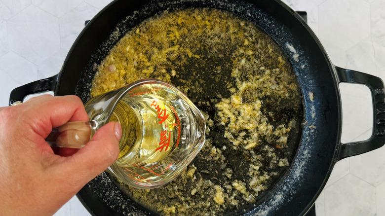 Hand holding measuring cup with white wine over large pan