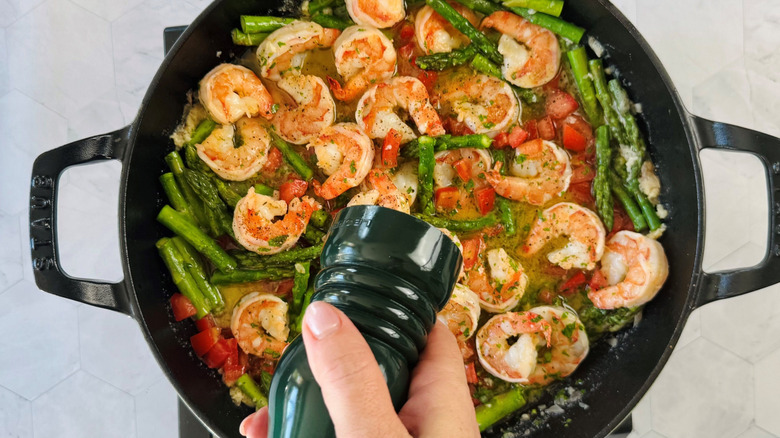 Hand holding pepper grinder over shrimp scampi in large pan
