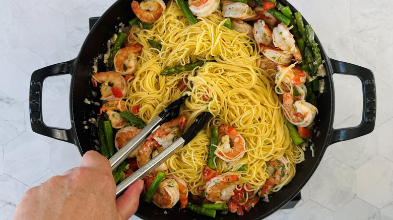 Tongs tossing pasta into a big pan of shrimp scampi