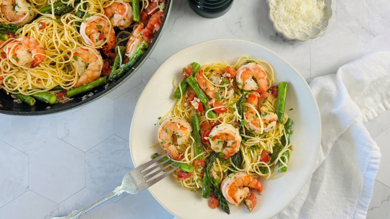Shrimp scampi serving on plate next to small bowl of Parmesan