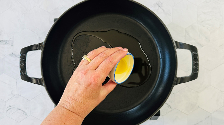 Hand pouring bowl of olive oil into pan