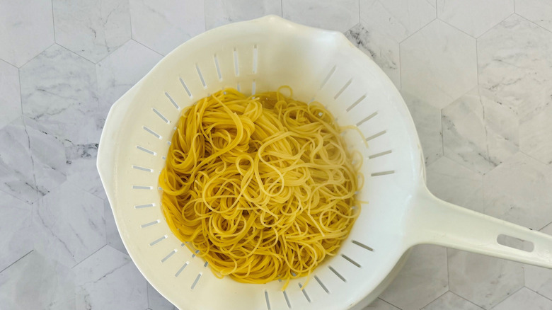Cooked angel hair pasta in colander on marble surface