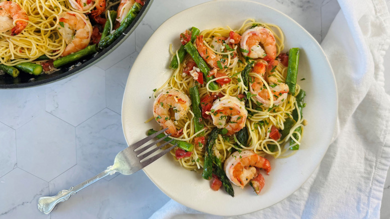 Shrimp scampi with asparagus and pasta on a white plate with metal fork