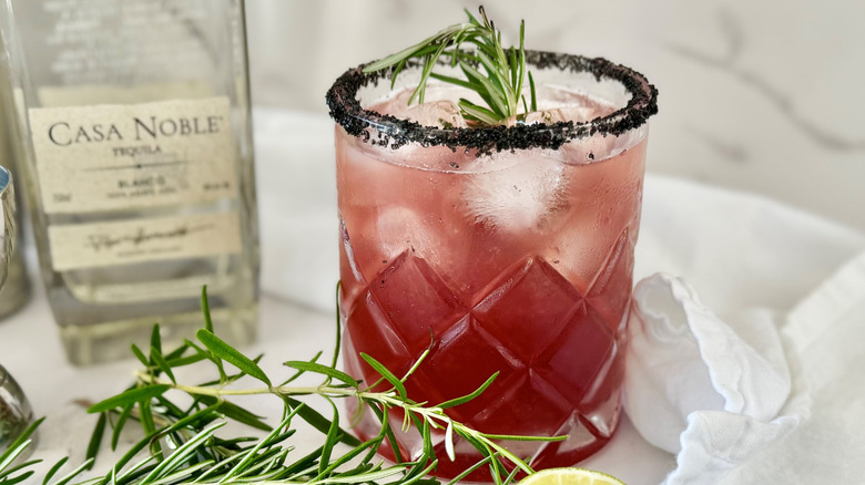 dark pink drink in a glass with ice and rosemary sticking out of the top