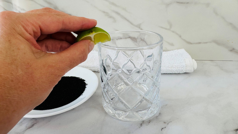 hand holding a piece of lime over a drinking glass