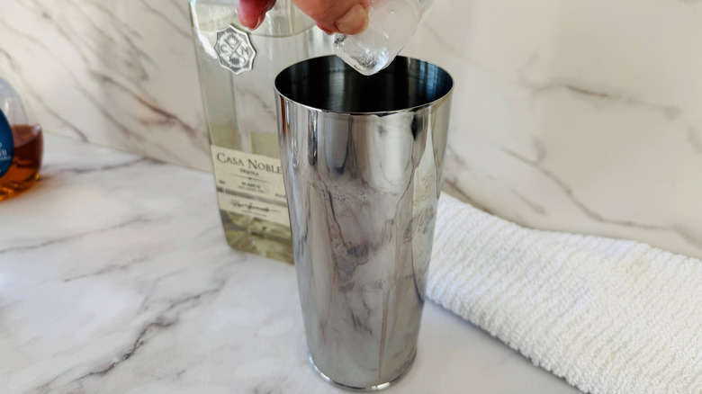 hand holding ice cubes over a cocktail shaker