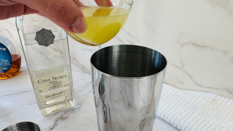 hand pouring lime juice into a cocktail shaker