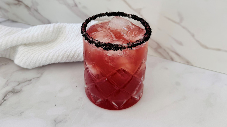 dark pink drink in a glass of ice with a black salt rim in front of a towel