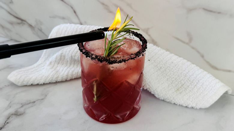 dark pink drink with flaming rosemary in front of a towel