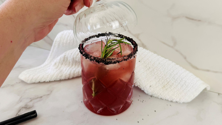 hand holding a stemmed glass over a dark pink drink in a stemless glass