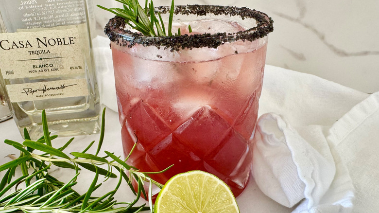 dark pink drink in a glass with ice and rosemary sticking out of the top