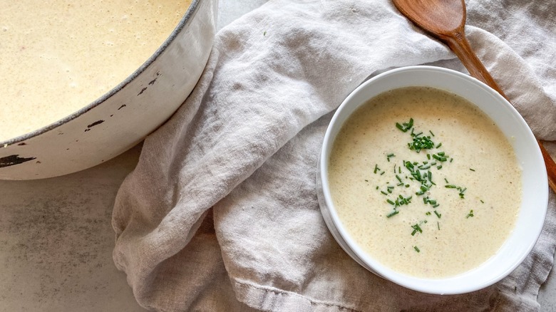 creamy potato soup in bowl with chives next to pot