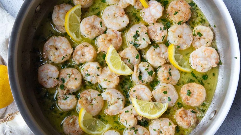 shrimp scampi with lemon slices in a metal skillet.