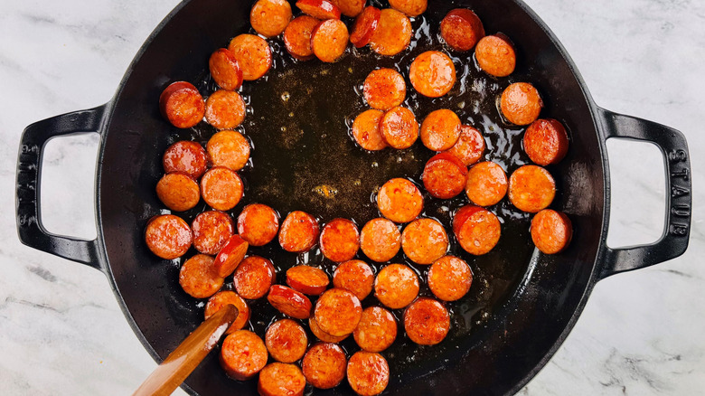sliced sausage in a black pot with a wooden spoon