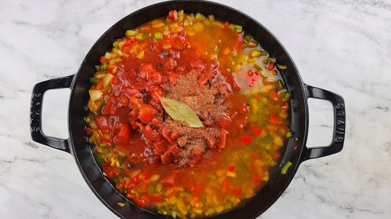 chopped vegetables and liquid in a black pot with spices and a bay leaf floating on the surface
