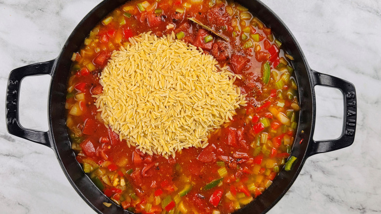chopped vegetables and liquid in a black pot with tiny pasta floating on the surface