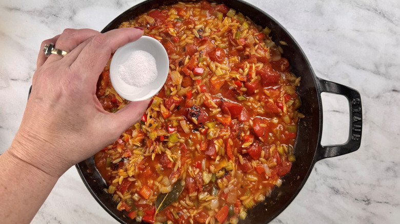 hand hovering salt over a pot of vegetables and pasta
