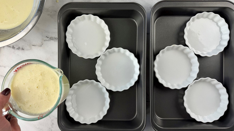 Custard mixture in measuring cup next to ramekins in baking dishes
