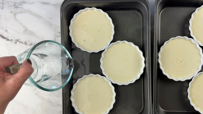 Water pouring into baking dish holding unbaked creme brulee ramekins