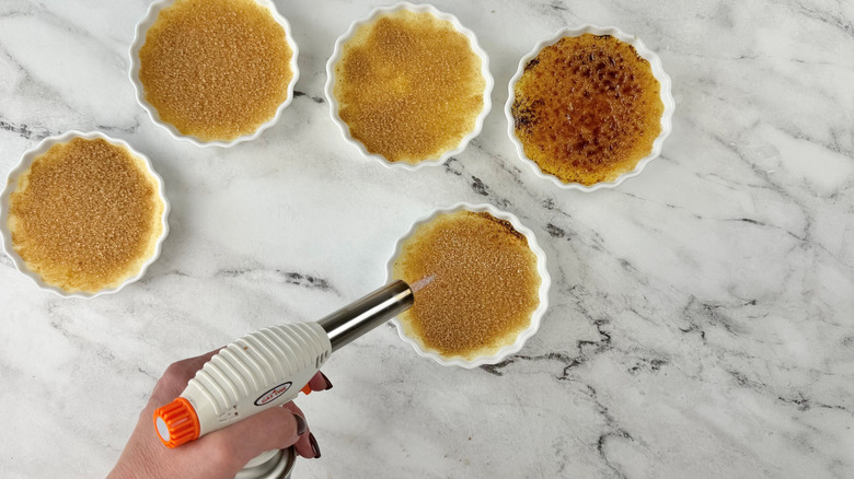 Hand using kitchen torch on creme brulee