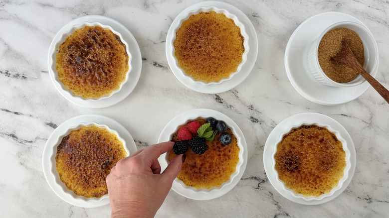 Hand adding berries to crème brûlée