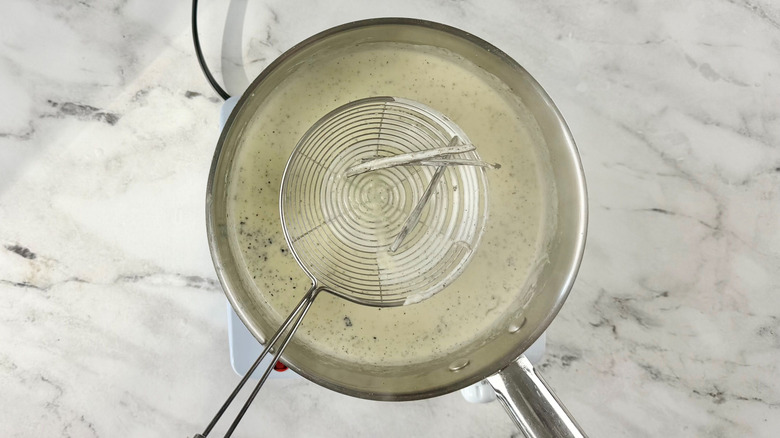 Strainer pulling vanilla pods out of cream mixture