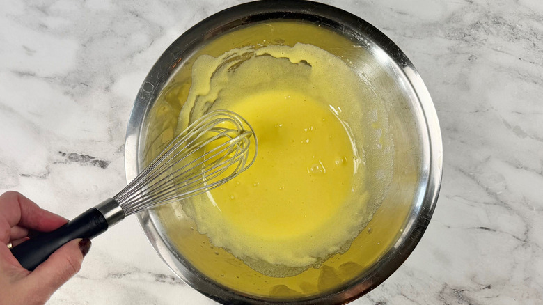 Hand holding whisk over yellow mixture in bowl