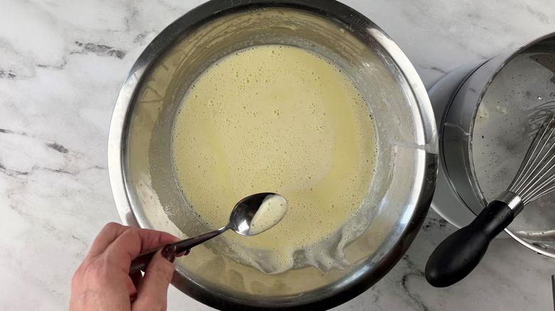 Spoon skimming bubbles off top of cream mixture in bowl