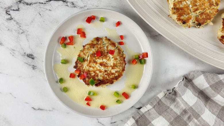Crab cake with lemon butter and diced peppers on plate