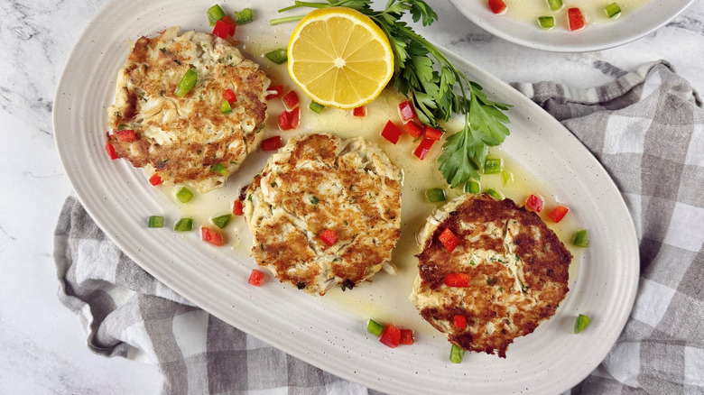 Crab cakes on serving platter with peppers, lemon and herbs