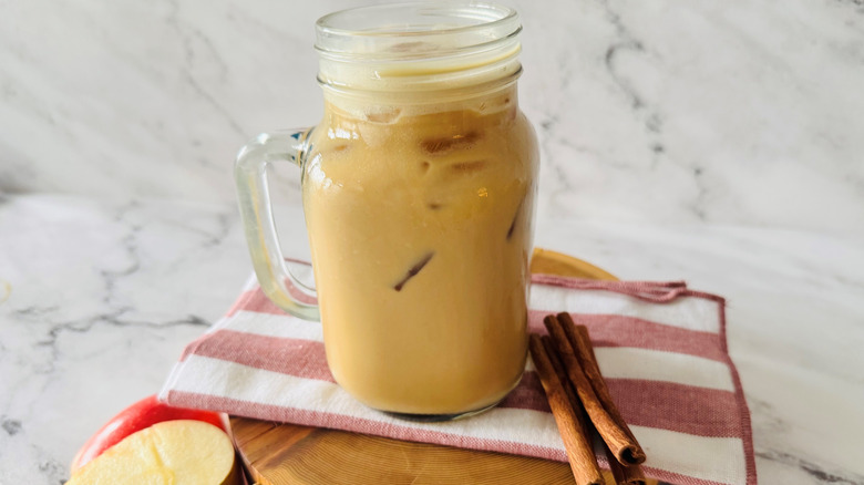 coffee drink in a mason jar-style mug posed next to cinnamon sticks and apple slices